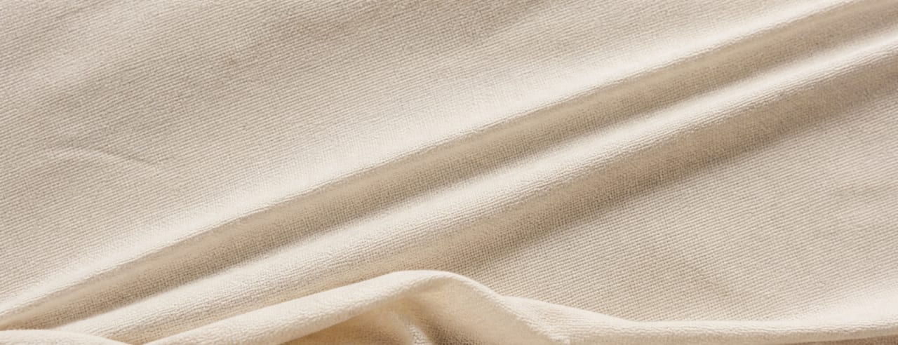 Drapé de coton crème tendu en oblique : deux lignes de force ascendantes et un pli relâché en bas, sous une lumière mi-dure.