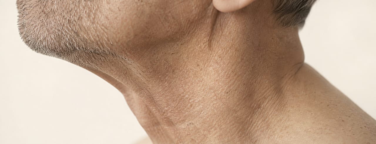 Profil d'un homme âgé : angle mandibulaire, ombre de barbe grise et relâchement du cou détourés par une lumière latérale arrière.