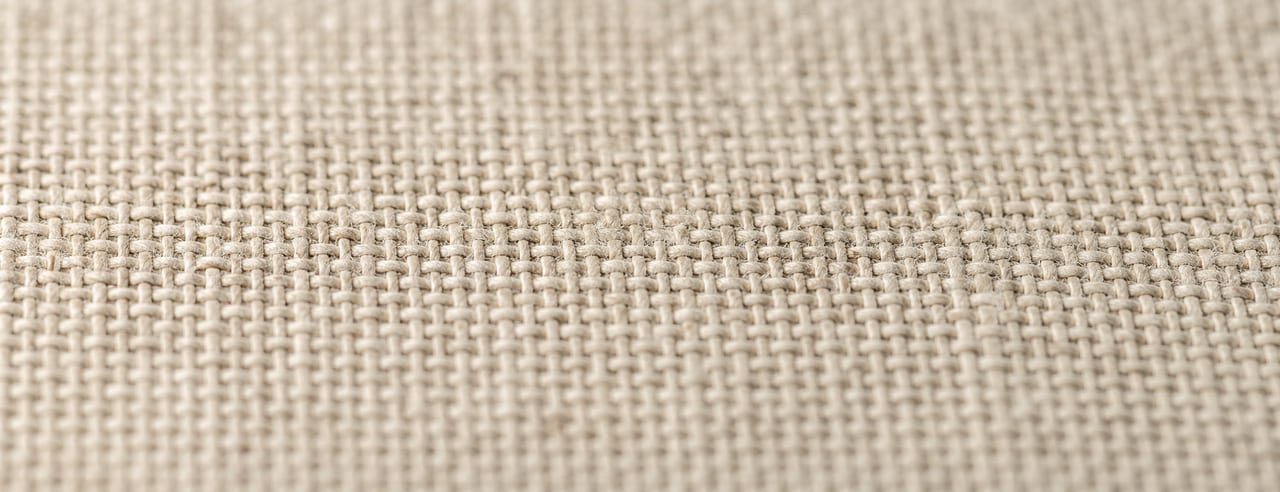 Lin lavé sable-ivoire au tissage dense, posé à plat, ombres des fils allongées par une lumière chaude très rasante.