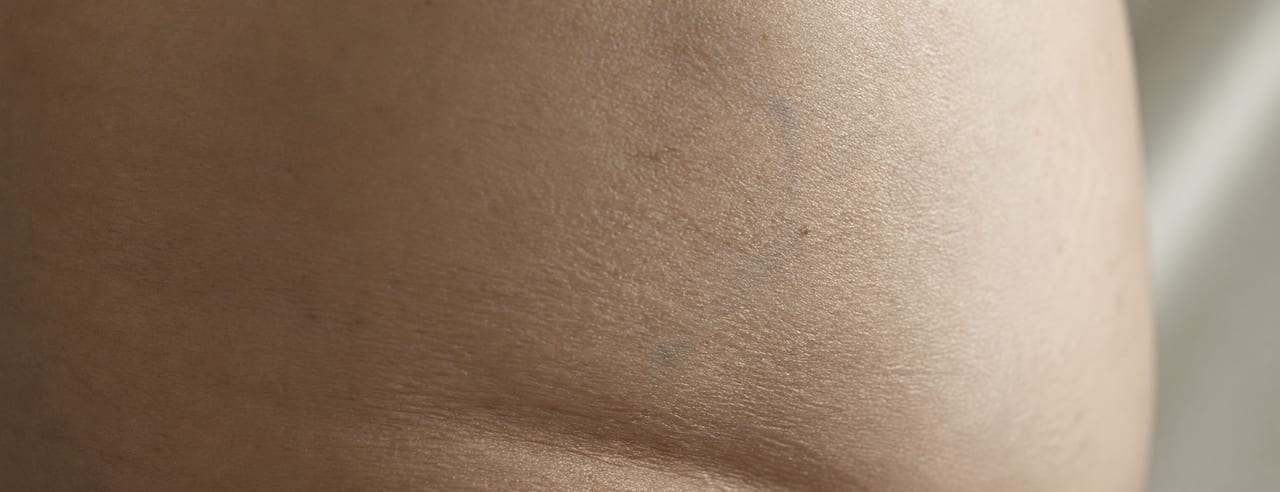 Surface cutanée du flanc vue de très près, micro-relief et légère ondulation naturelle détachés par une lumière rasante.