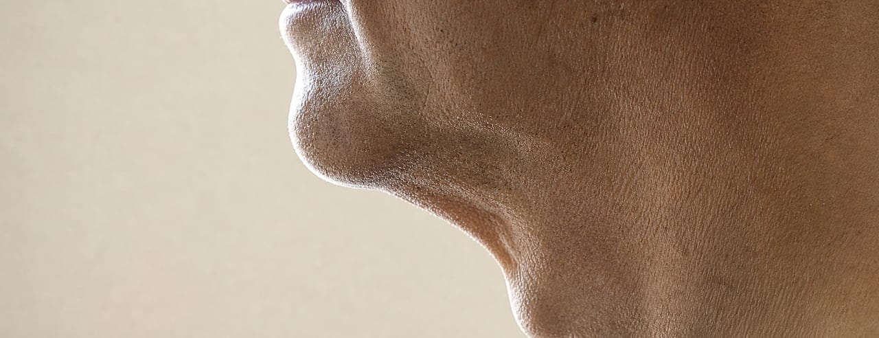 Profil du tiers inférieur d'un visage masculin, menton et ligne mandibulaire détourés par une lumière arrière presque en découpe.