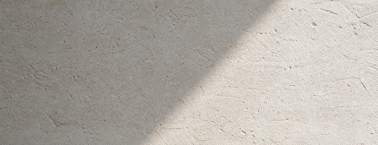 Mur de pierre calcaire claire et nu, tache de lumière du matin sur le tiers droit, frontière ombre-lumière en oblique douce.